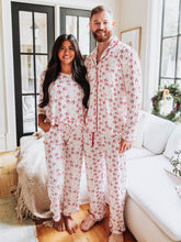 This festive unisex pajama set features a cheerful Santa Claus print scattered across a soft white background with bright red accents along the buttons, piping, and drawstring. The playful all-over St. Nick brings a touch of nostalgia and fun to your holiday sleepwear collection. Made from cozy, breathable fabric, these unisex Christmas pajamas are perfect for lounging, family photos, or Christmas morning gift opening.